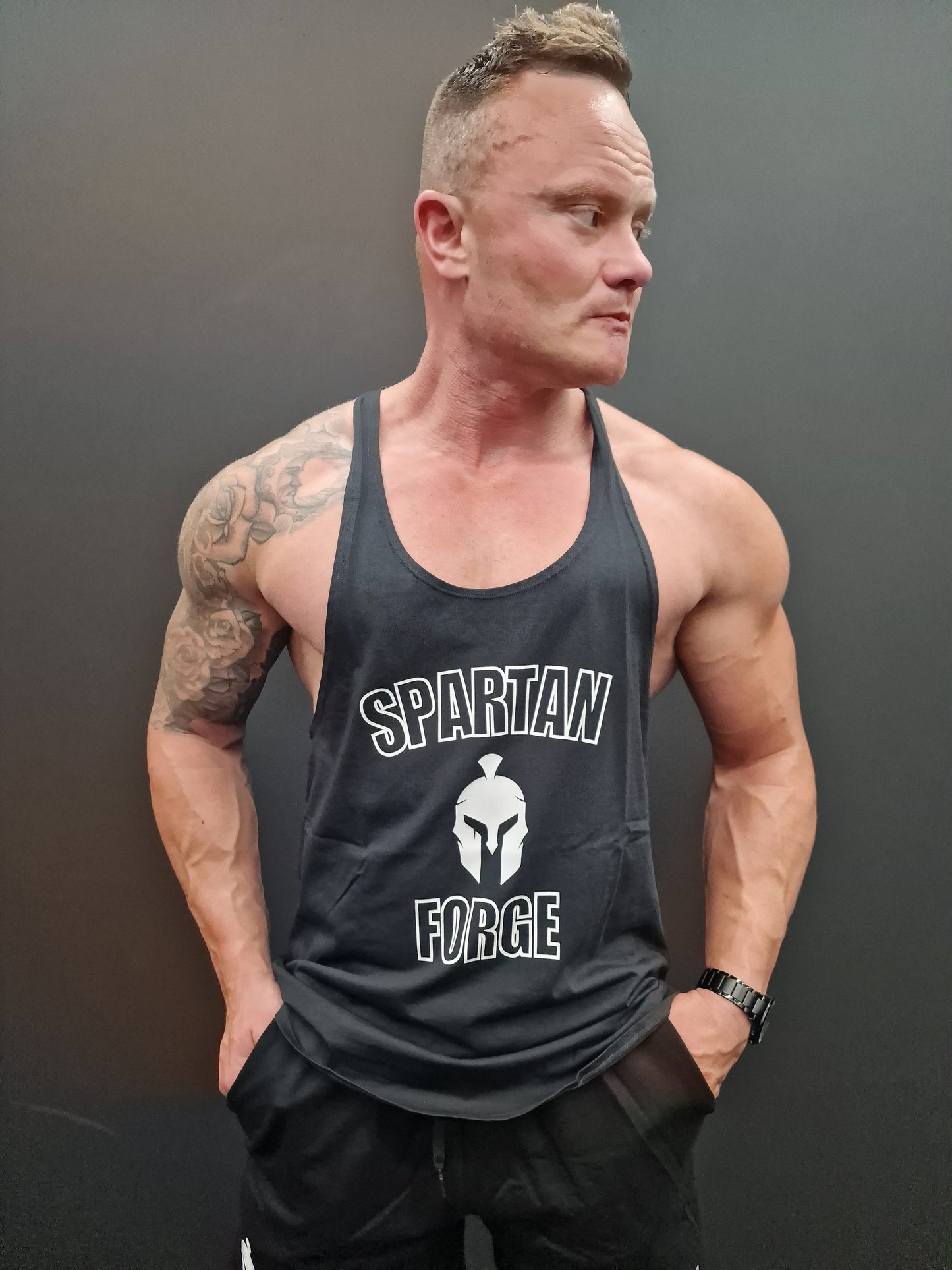 Man wearing a black tank top with 'Spartan Forge' logo against a gray background