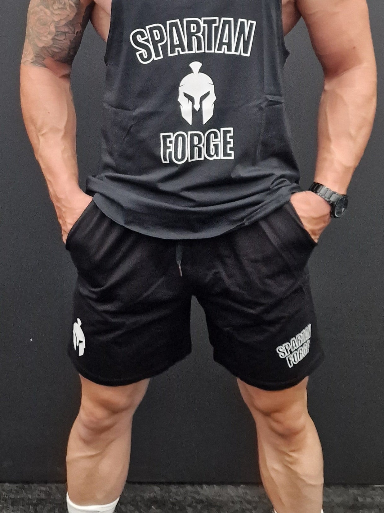 Man in athletic wear standing on a black mat against a gray wall