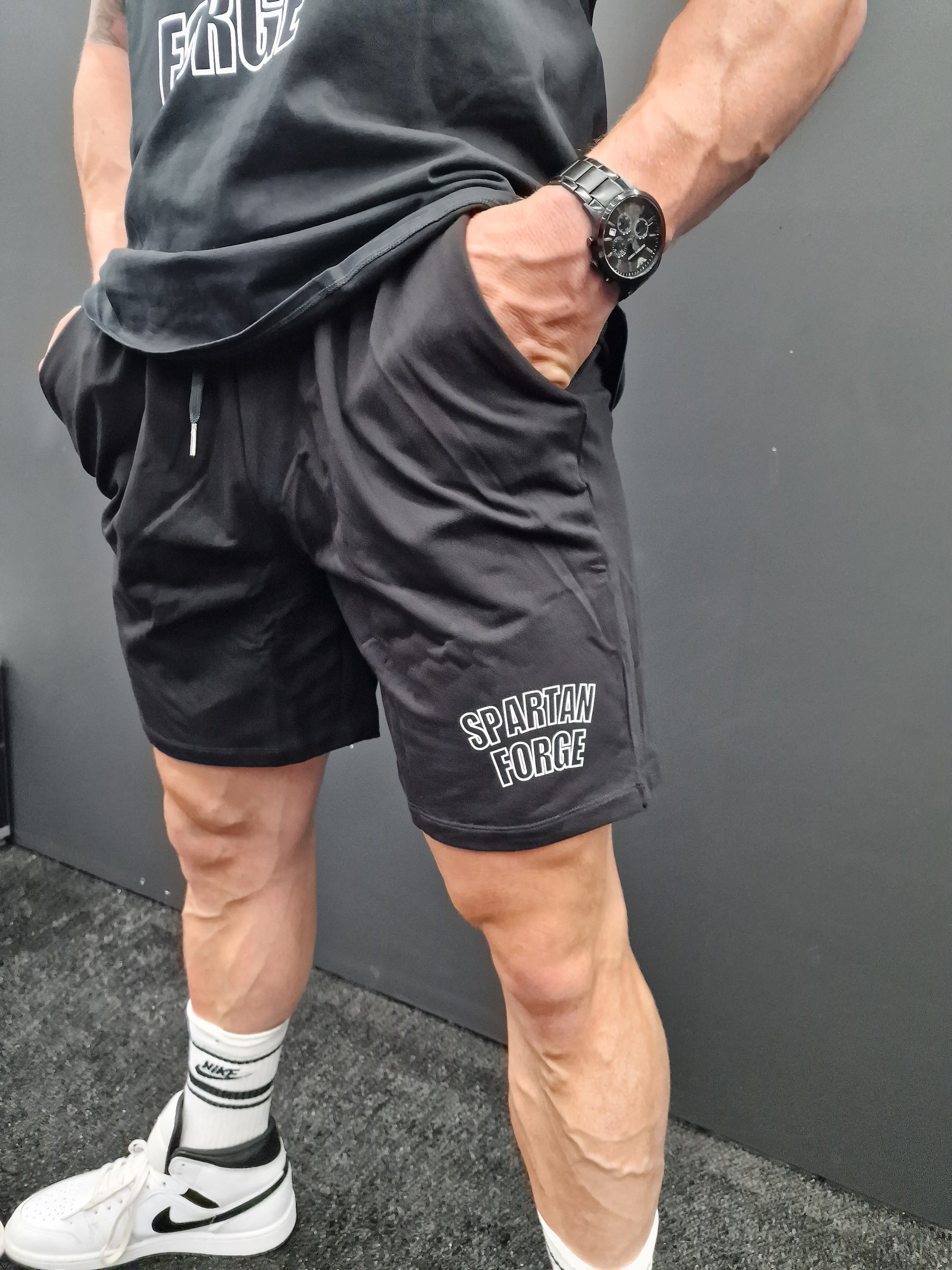 Person wearing black shorts with 'Spartan' branding, standing on a gray floor.