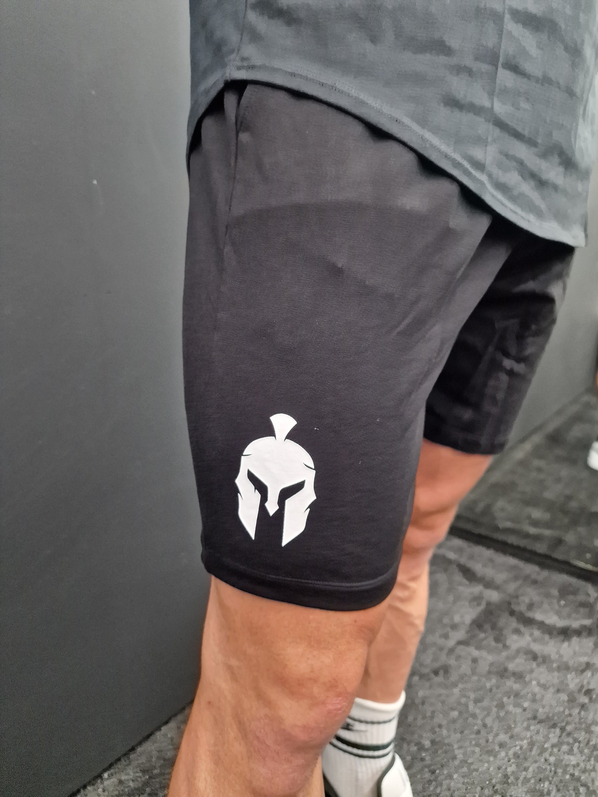 Person wearing black gym shorts with a white spartan helmet logo printed on the leg