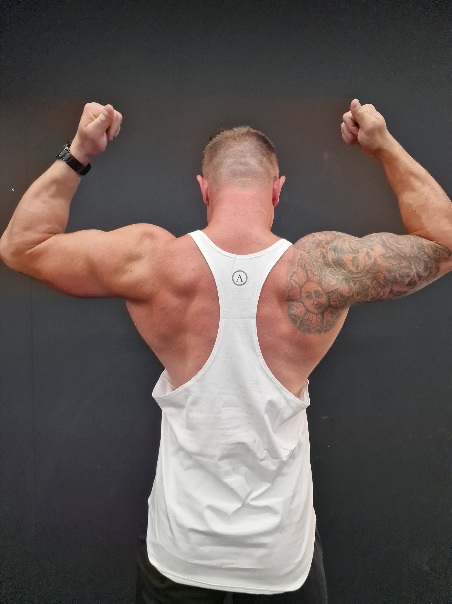 Man in a white tank top with tattoos on his arms against a dark background